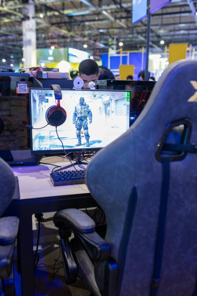A gaming station featuring a high-end monitor, gaming chair, and headphones at a vibrant tech convention.